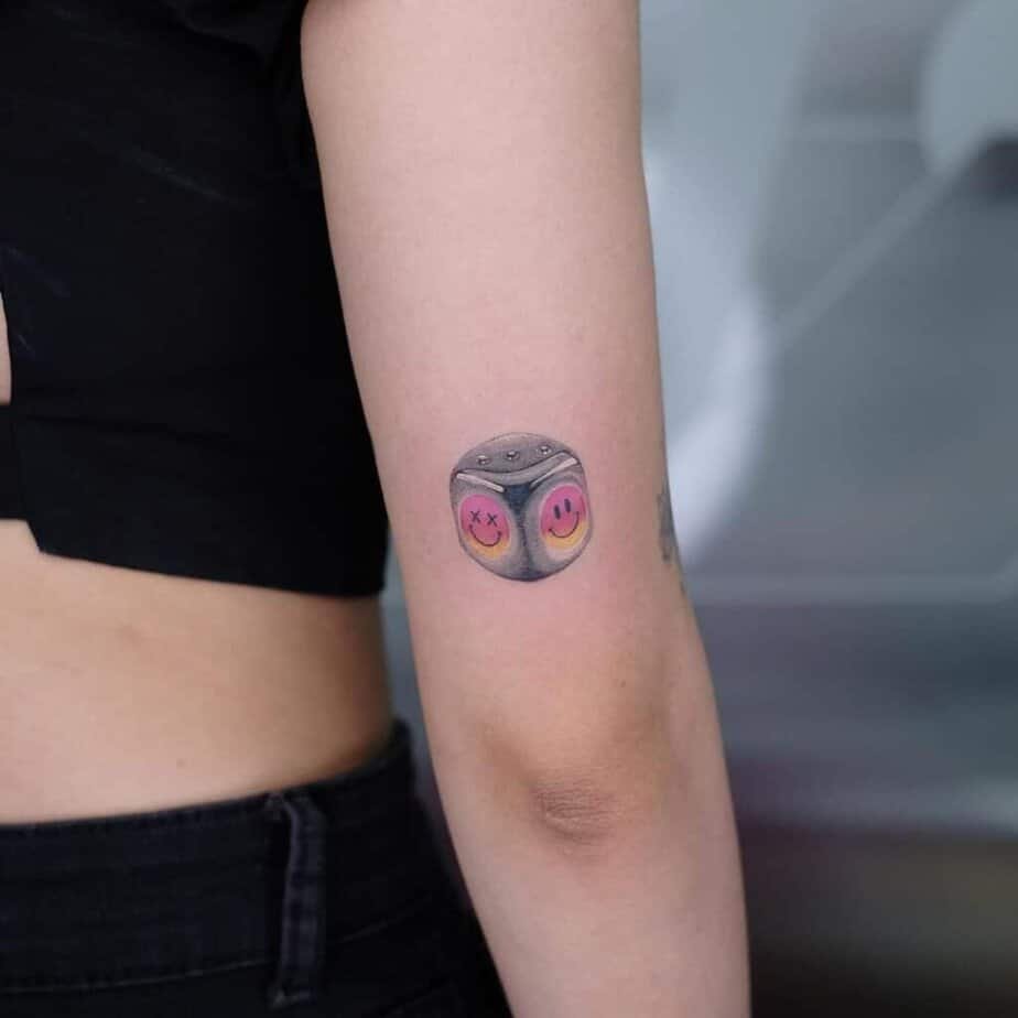 17. Dice tattoo with a smiley face on the back of the arm