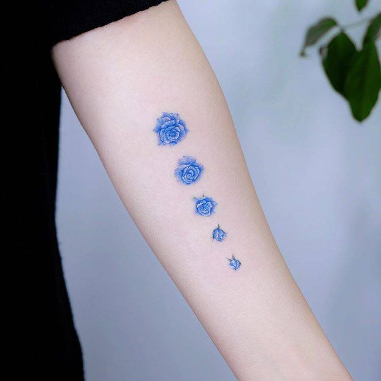 Forearm tattoo of a blue rose at different blooming stages