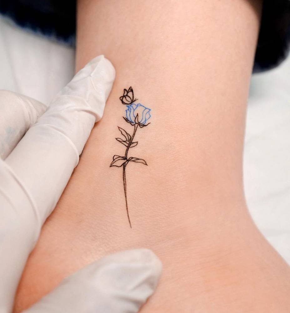 Ankle tattoo of a butterfly landing on a blue rose
